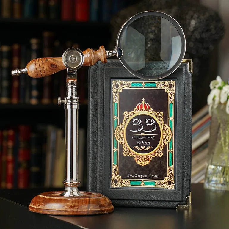Настільна лупа та книга «33 стратегії війни» у шкіряній обкладинці